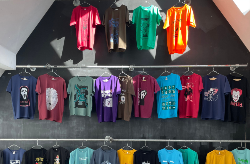 An einer Wand hängen viele bunte, bedruckte T-Shirts