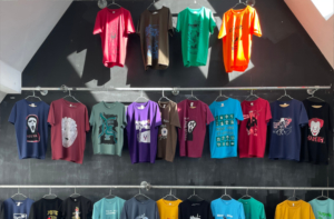 An einer Wand hängen viele bunte, bedruckte T-Shirts