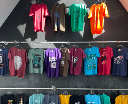 An einer Wand hängen viele bunte, bedruckte T-Shirts