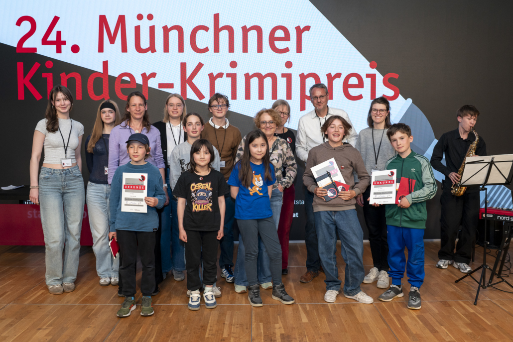 Das Foto zeigt die sechs Preisträger*innen und die Jury-Mitglieder bei der Verleihung des Kinder-Krimipreises 2026