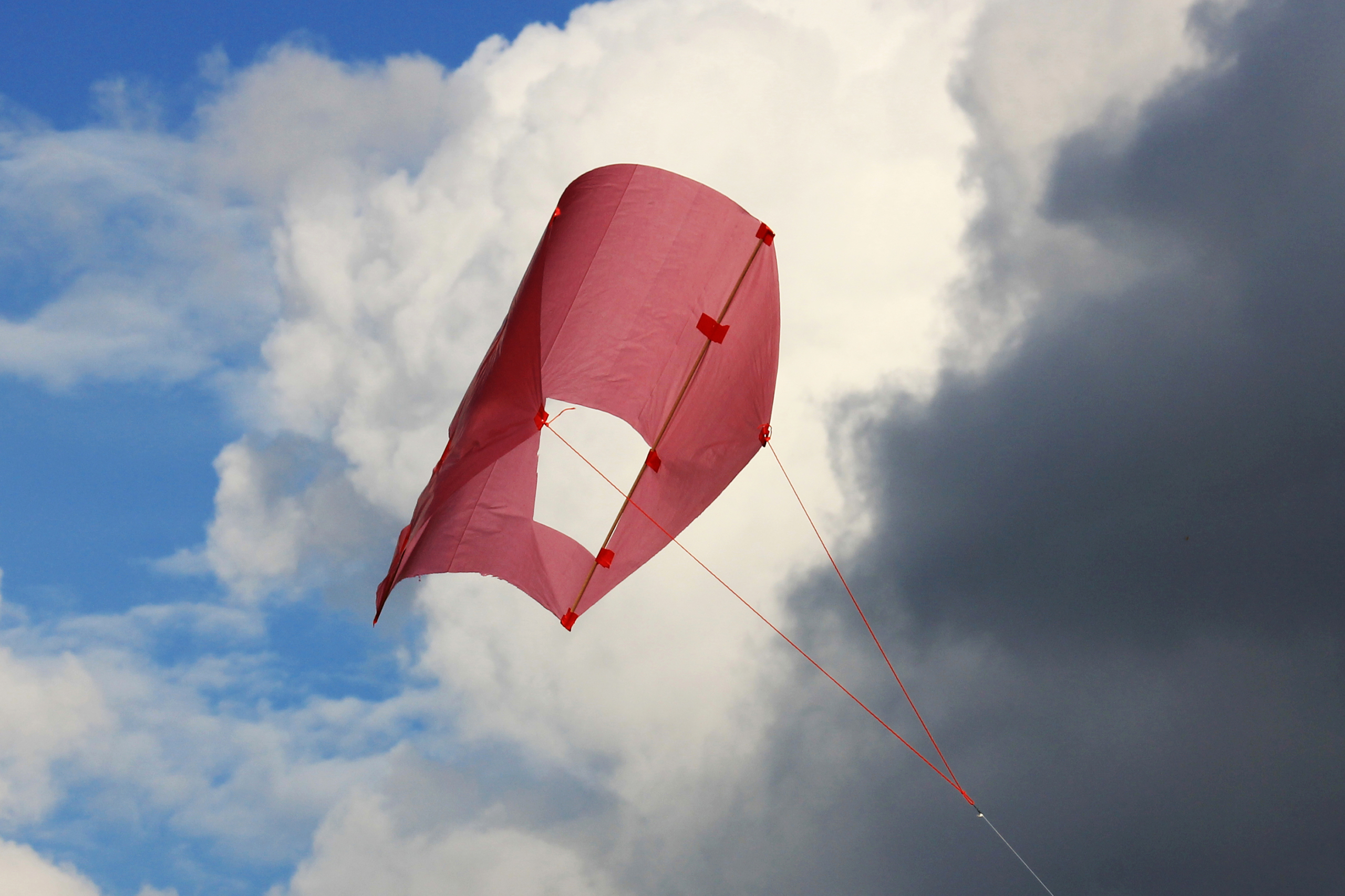 Sled vor Wolken_ak25 Vor bewölktem Himmel steigt ein roter Kastendrachen in die Luft.