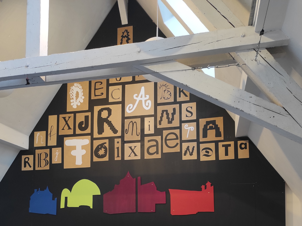 An der Giebelwand eines Werkstattraums hängen Buchstaben in unterschiedlichen Farben und Designs.