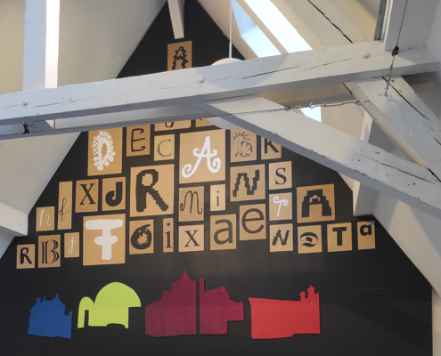 An der Giebelwand eines Werkstattraums hängen Buchstaben in unterschiedlichen Farben und Designs.